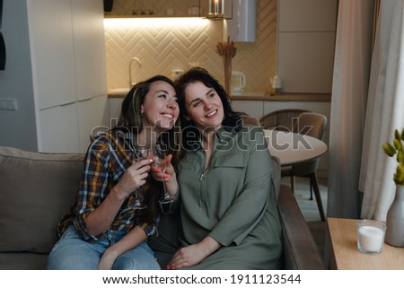 Two female friends are sitting on the couch, raising their glasses and looking out the window.