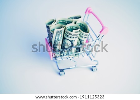 miniature shopping cart filled with one dollar banknotes on white background