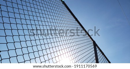A bottoms up view with the perspective of looking up through a chain link metal fence. The sun is glaring through the mesh and an electrical line is in the distance. Angled and textured background pic Royalty-Free Stock Photo #1911170569