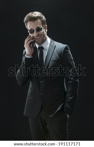 handsome man in black suit using a phone  on a black background