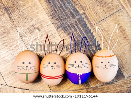 Easter eggs, cute bunny face painted on eggshells with multicolor fancy costume party concept on wooden texture background. Creative idea of fun and happy traditional holiday in April. Top view