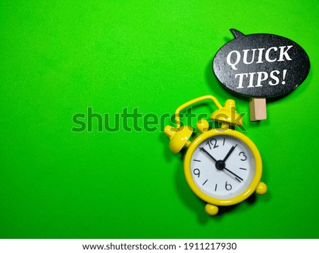 Selective focus.Alarm clock and wooden board with written text QUICK TIPS.Business concept.Shot were noise and film grain.