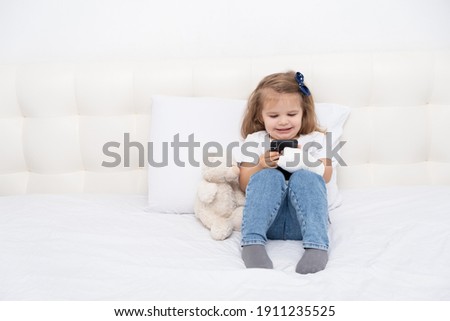 Little girl with hand in cast sitting in bed using smartphone, watching cartoon or education video.