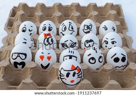 Painted eggs with faces and emotions in egg tray.