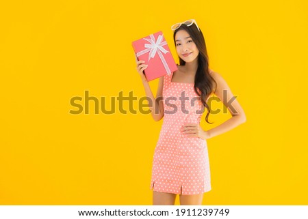 Portrait beautiful young asian woman with red gift box on yellow isolated background