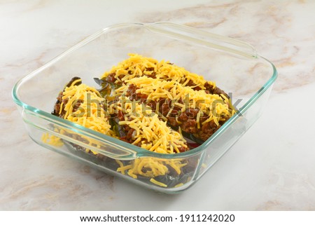 Preparing stuffed poblano peppers in glass baking dish by adding shredded cheese on top