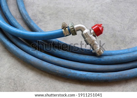 Metal hose clamp is tightening to faucet red handle with blue rubber hose on cement flooring background closeup.