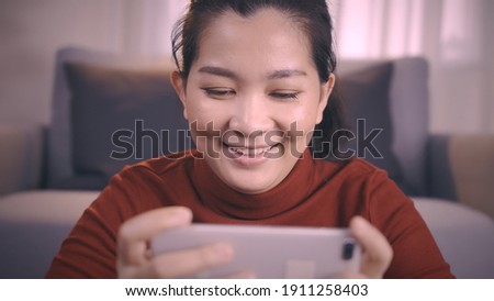 Asian women on redshirt using a smartphone for gaming online with excited emotion in living room