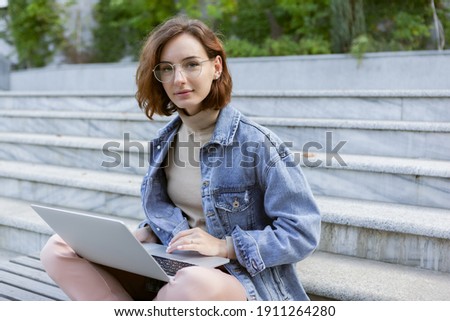 Young pretty student woman sitting with laptop. Caucasian girl working or study with notebook outdoors.