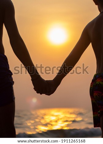 Brother and younger brother holding hands on the beach with evening sunset background