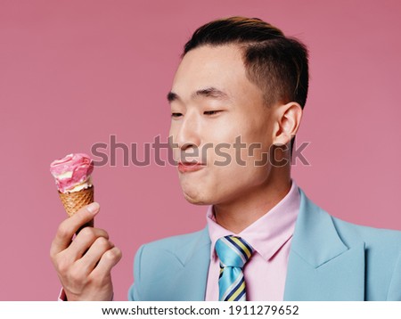 asian man with ice cream in cone on pink background and blue suit model cropped view