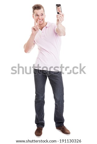 Full length portrait of a happy young man showing a peace sign and taking a SELFIE - isolated on white