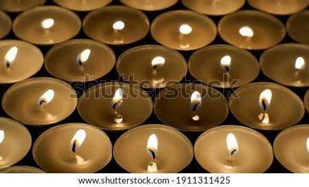 Many burning round small candles with reflections are burning in dark. Fire background. Selective focus. Close-up.