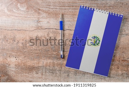Notepad with Salvador flag, pen on wooden background, study concept