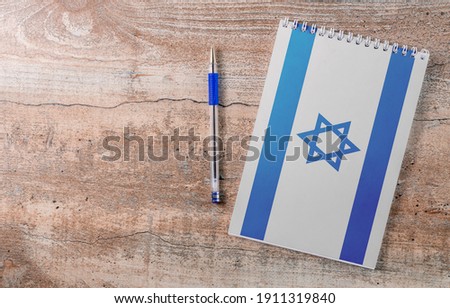 Notepad with Israel flag, pen on wooden background, study concept Royalty-Free Stock Photo #1911319840