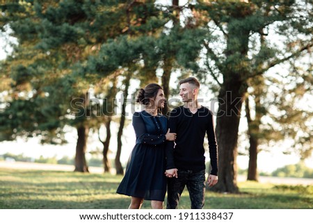 Young couple in love walking in the summer park holding hands. woman and man dressed in black clothes have a date outdoors. Romantic relationship. Valentines Day.