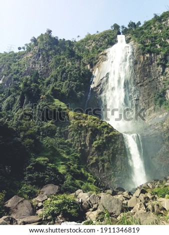 Low angle picture of stunning waterfall cascaded down the jagged mountain rocks along with green nature.