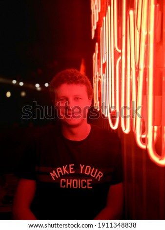 Bar owner young man in light of red neon lettering or sign. Portrait, vertical photo, selective focus. Make your choice