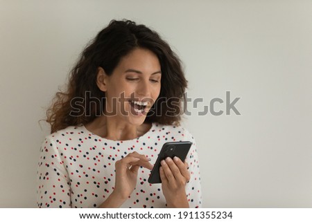 Overjoyed millennial woman isolated on grey studio background look at cellphone screen win online lottery. Happy young female feel euphoric triumph read good pleasant message or news on smartphone.