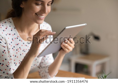 Close up of smiling young woman look at table screen shopping online on modern device from home. Happy millennial female work distant or study on internet on pad gadget. Technology concept.