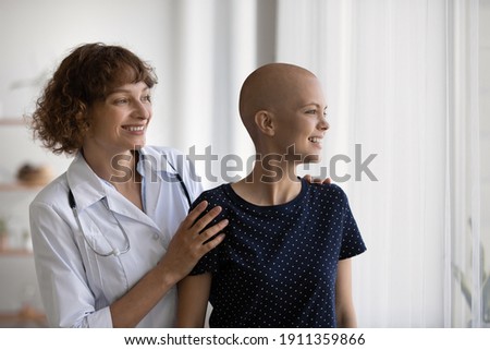 Smiling Caucasian doctor or nurse support comfort millennial woman struggle with oncology. Happy GP and optimistic female cancer patient look in distance dream of illness recovery or remission. Royalty-Free Stock Photo #1911359866