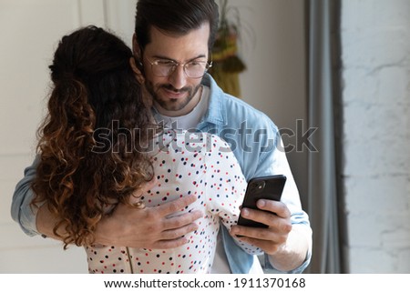 Lack of trust in relations. Suspicious jealous boyfriend hug girlfriend checking her phone calls contacts behind back. Unfair husband cheating wife simulate love while reading messages from mistress Royalty-Free Stock Photo #1911370168