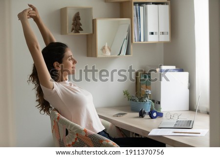 With great relish. Serene female student relaxing after long time of distant learning by laptop at home office. Happy young woman satisfied with finishing work on pc stretch muscles lean back on chair Royalty-Free Stock Photo #1911370756