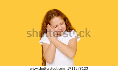 Sad little girl with earache on a yellow background. Ear ache concept. Royalty-Free Stock Photo #1911379123