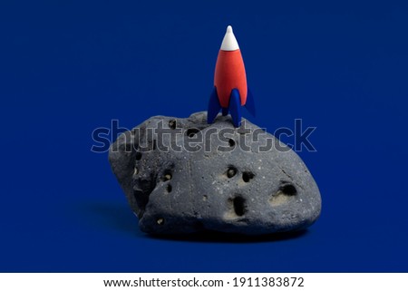 Cute miniature rocket on a moon stone on a dark blue background. Minimal space day card. 