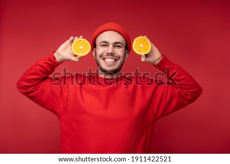 Photo of happy man with beard in red clothing. Holds orange and smiles, isolated over red background