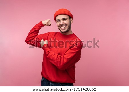 Photo of attractive man with beard in glasses and red clothing. Male show strong and muscles, isolated over pink background