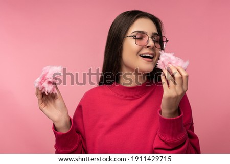 Photo of attractive lady in glasses plays with cotton candy sweet has fun happy wear casual pink sweater isolated pink color background