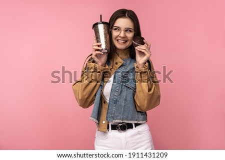 Photo of attractive lady holds tea coffee and muffins, happy wait for something, wear casual jeans jacket white undershirt isolated pink color background