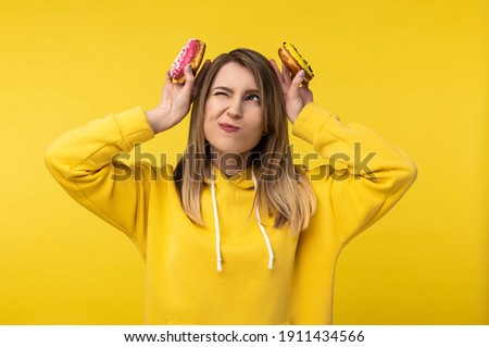 Photo of attractive lady holds donuts behind her head pretend being bunny. Wears casual yellow hoody, isolated yellow color background