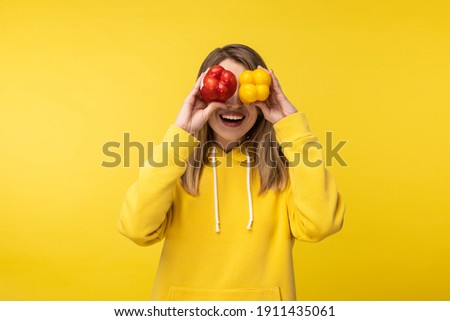 Photo of attractive lady holds papers and covers eyes up with smile. Wears casual yellow hoody, isolated yellow color background