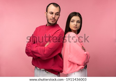 Photo of attractive man wih beard in red clothing and woman in pink stand and pose for camera glare on each other, isolated over pink background