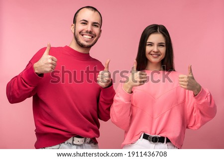 Photo of attractive man wih beard in red clothing and woman in pink show thumb up and smile, isolated over pink background
