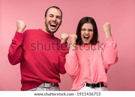 Photo of attractive man wih beard in red clothing and woman in pink smile and rejoice something. Couple looks funny, isolated over pink background