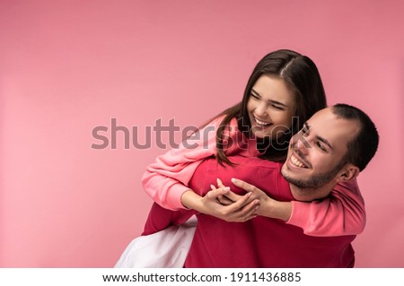 Photo of sweet couple hug each other and smile. Male and female are in love, isolated over pink background