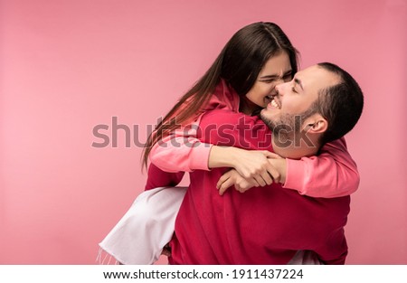 Photo of sweet couple hug each other and smile. Male and female are in love. Woman tries to bite man. Isolated over pink background