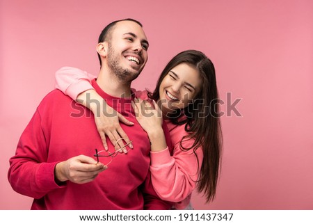 Photo of sweet couple hug each other and smile. Male and female are in love look blessed, isolated over pink background