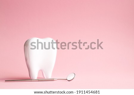 White tooth with dental mirror on pink background in honor of international dentist day with place for text Royalty-Free Stock Photo #1911454681