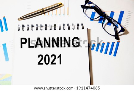 In the notebook text Planning 2021, next to glasses and pen, the background are graphics and reports.