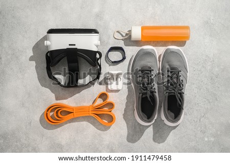 Fitness, workout, and VR technology concept. Sports equipment on grey background: virtual reality glasses, expander, fitness tracker, sneakers, juice. Knolling flat lay composition, top view Royalty-Free Stock Photo #1911479458