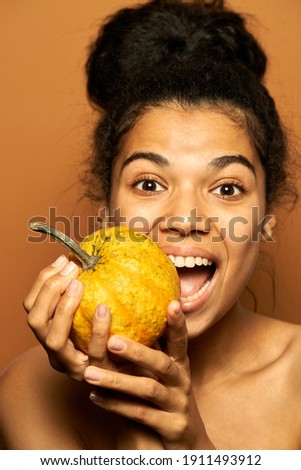 Fresh squash. Portrait of excited young mixed race female model looking at camera, holding little pumpkin, posing isolated over orange background. Healthy eating, skincare concept