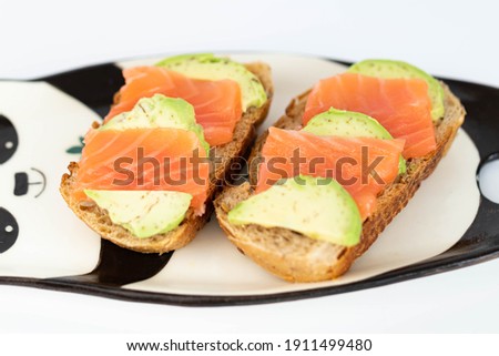 Homemade toast sandwich with salmon and avocado on a slice of cereal bread. The toast lies on a plate in the shape of a black and white panda. healthy food