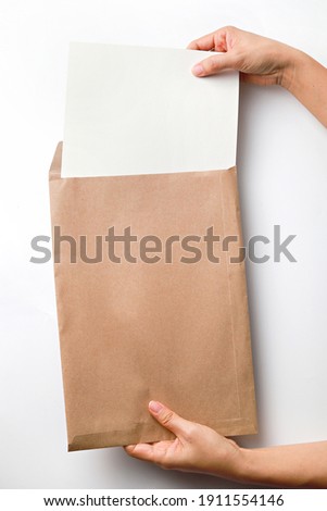 Female's hands holding brown kraft paper envelope with blank white paper over white background.