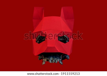 A red mask is worn on a black skull on a red background. Stylish and beautiful red animal mask with ears on a red background. Mask of a wolf, fox, dog, cat.