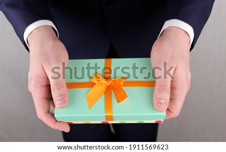 A gift in a green gift box in the hands of a man in a blue suit. Congratulations to the woman. Women's day, birthday, mother's day