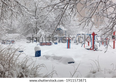 It is snowing and creating large drifts. Fresh snow cover, snow-covered trees and a playground.